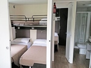 Habitación compacta con literas, baño pequeño con inodoro y lavamanos, y zona de ducha.