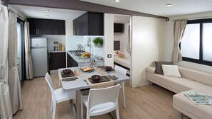 A compact living space with a kitchenette, dining area, and a sofa. - Camping Village I Tre Moschettieri (Comacchio)