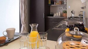 A modern kitchen with dark cabinets, a gas stove, a sink, and a breakfast setup including a muffin, glasses, and a fruit bowl. - Camping Village I Tre Moschettieri (Comacchio)