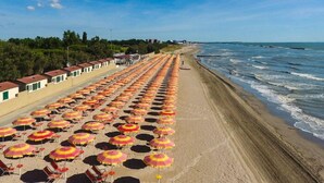 A beach with rows of beach umbrellas and chairs, a sandy shore, and a clear blue sky. - Camping Village I Tre Moschettieri (Comacchio)
