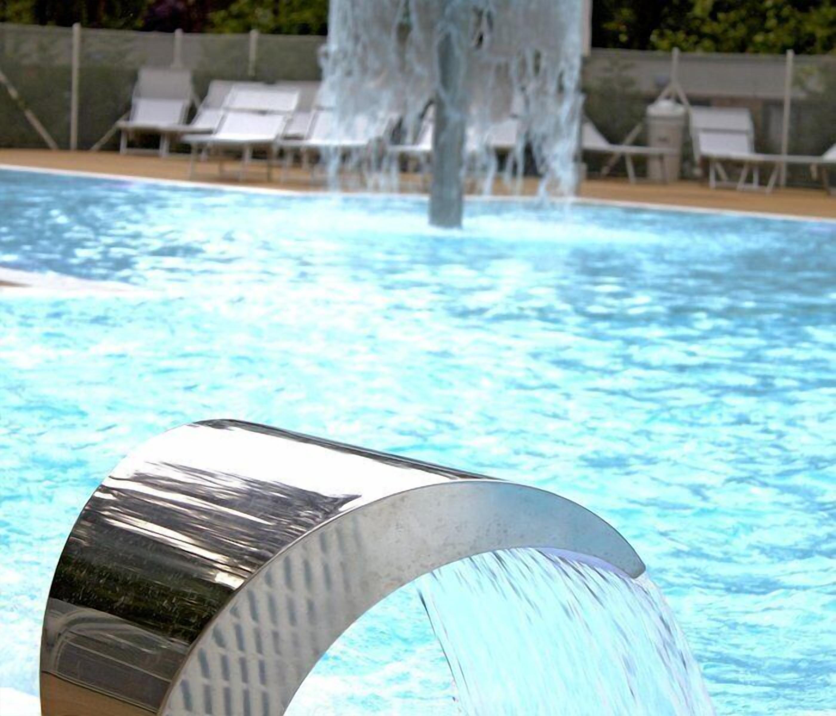 Una piscina con cascata e sedie a sdraio sullo sfondo.