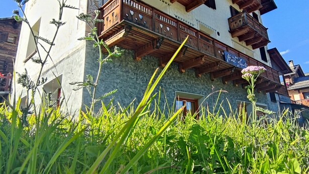A hotel with multiple balconies, a stone facade, and lush greenery in the foreground. - Hotel Aquila (Livigno)