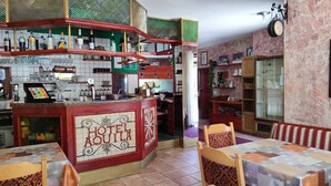 A hotel bar with a tiled backsplash, a counter with a 'HOTEL AQUILA' sign, and a seating area with patterned chairs and a table. - Hotel Aquila (Livigno)