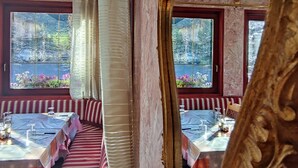 A room with a long, striped sofa, a large ornate mirror, and a view of a garden through a window. - Hotel Aquila (Livigno)