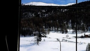 A snowy landscape with a cabin and trees through a window with a wooden frame. - Hotel Aquila (Livigno)