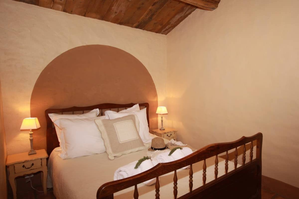 Une chambre à coucher avec un lit en bois, deux lampes de chevet et une grande fenêtre en arc de cercle.
