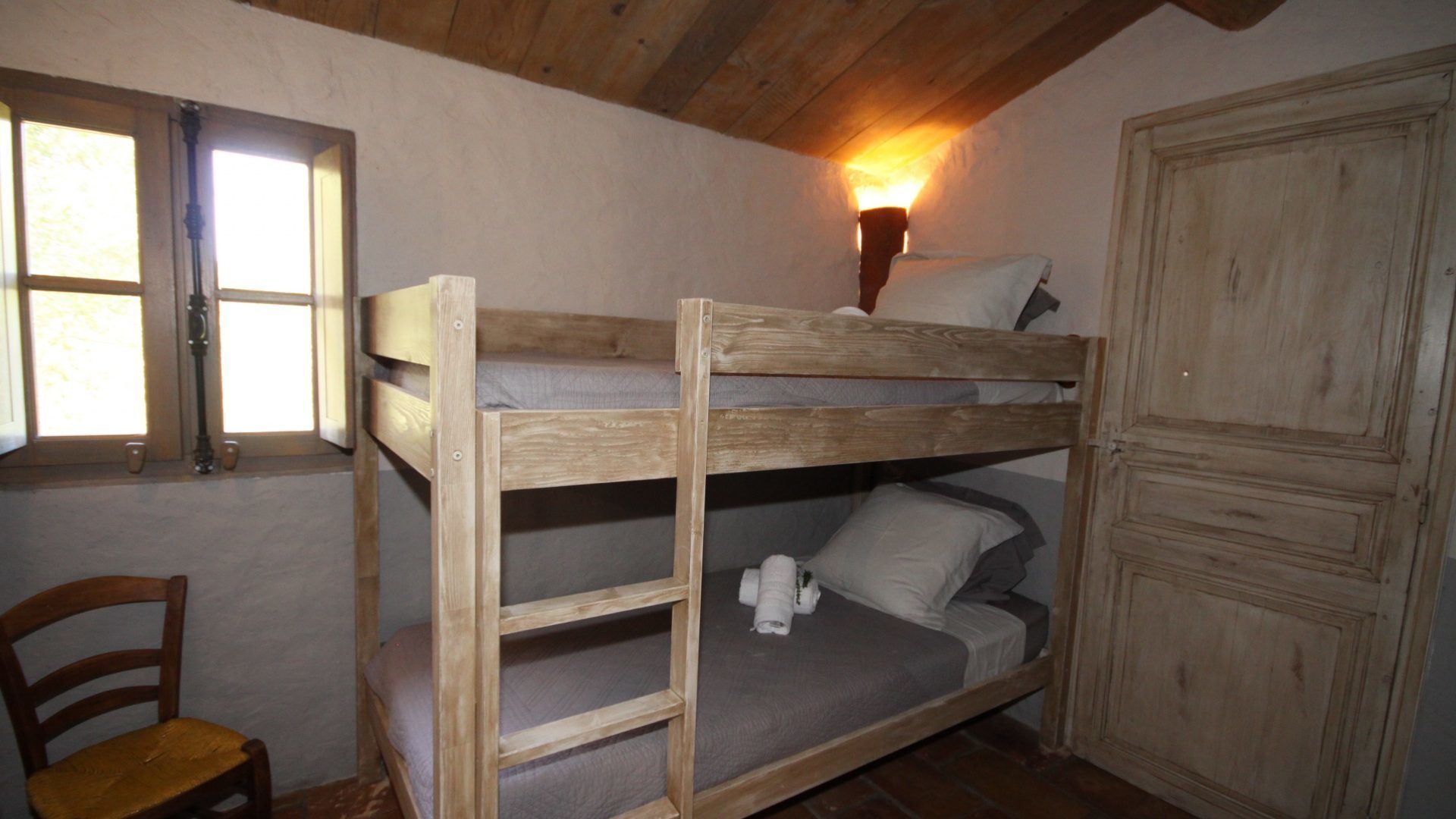 Dormitorio con literas, techo de madera, una ventana y un armario.