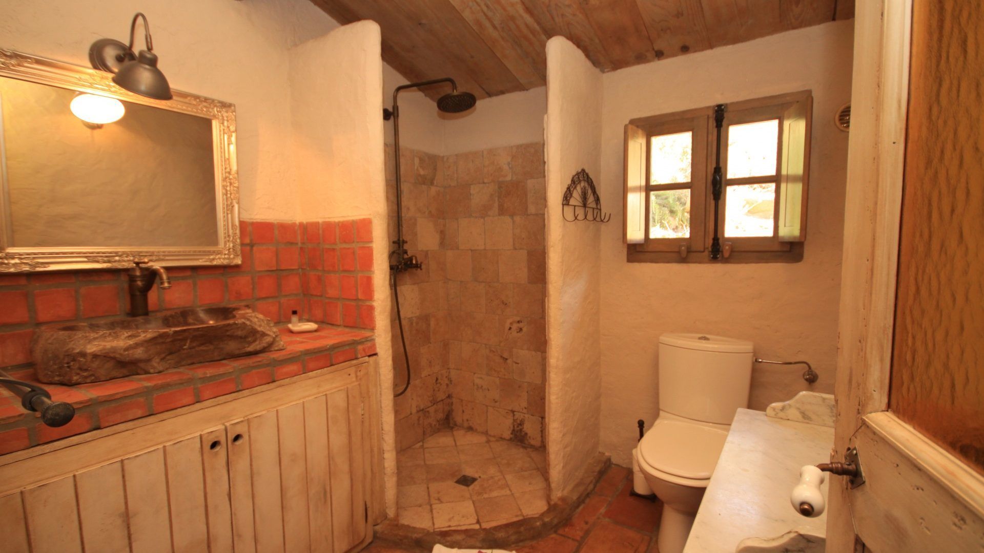 A bathroom with a stone shower, a wooden vanity, and a white toilet.