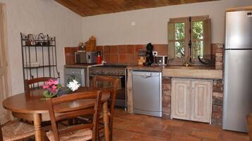 A compact kitchen with a wooden table, chairs, a stove, a microwave, a toaster, and a refrigerator.