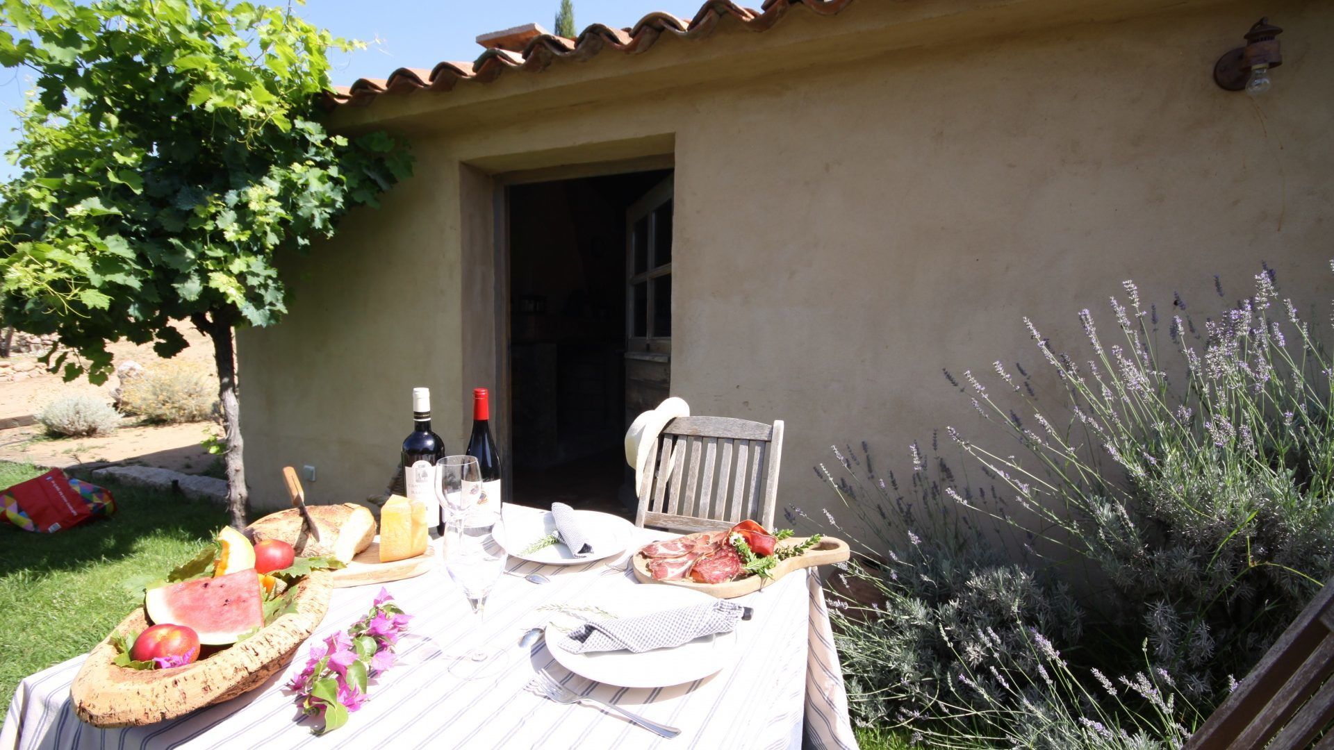 An outdoor dining area with a table set for two, featuring a bottle of wine, bread, and a salad.