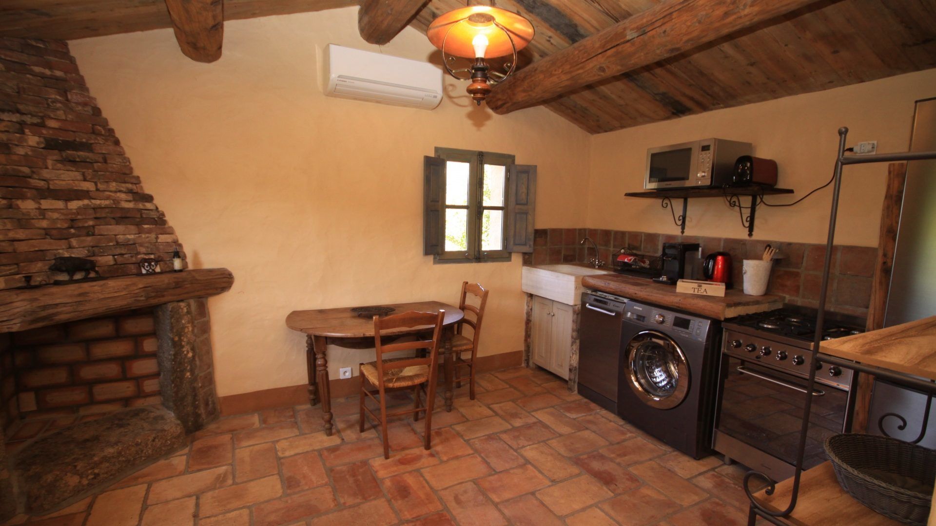 Cocina funcional con lavadora, microondas y estufa. Incluye mesa de comedor con sillas y lámpara colgante.
