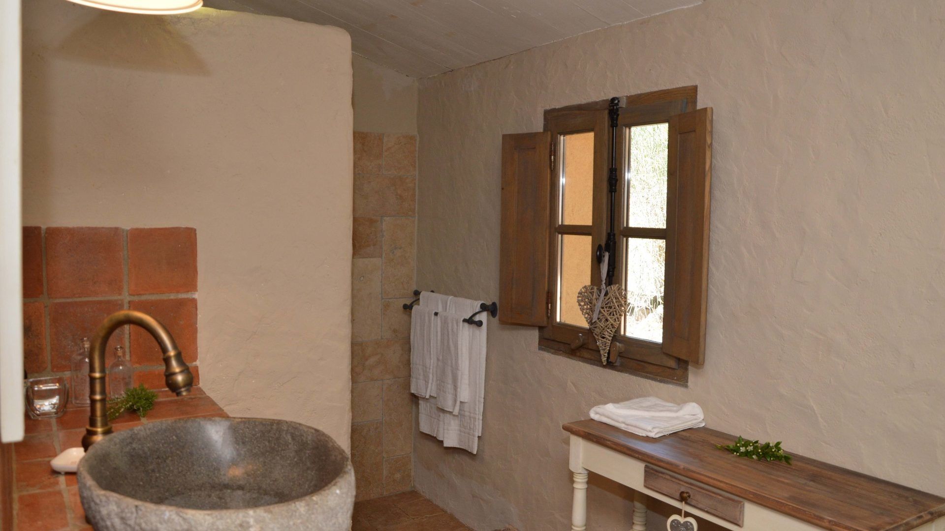 A bathroom with a stone sink, a wooden window, and a small wooden vanity.