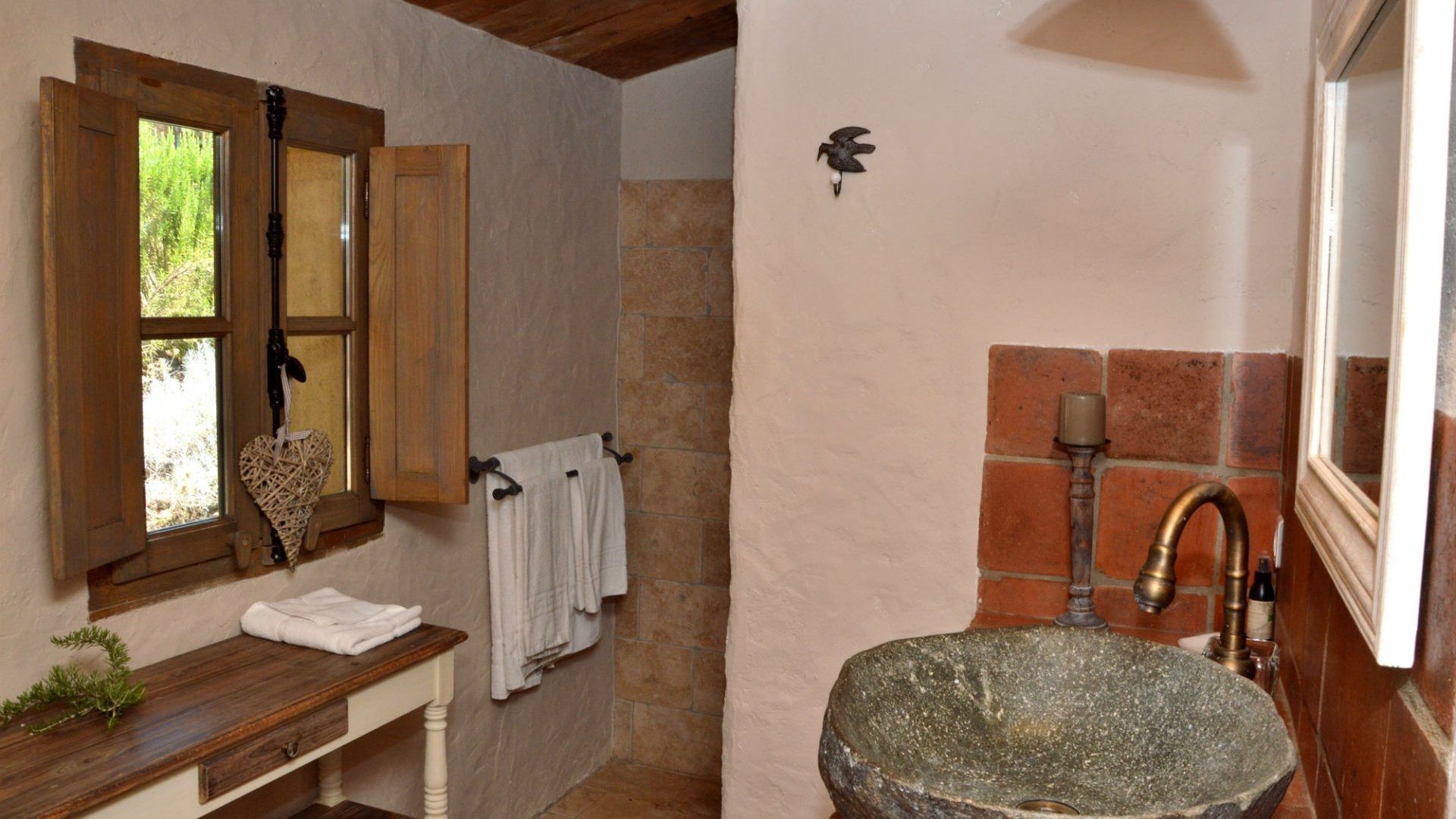 A rustic bathroom with a stone sink, wooden window frames, and a towel rack.