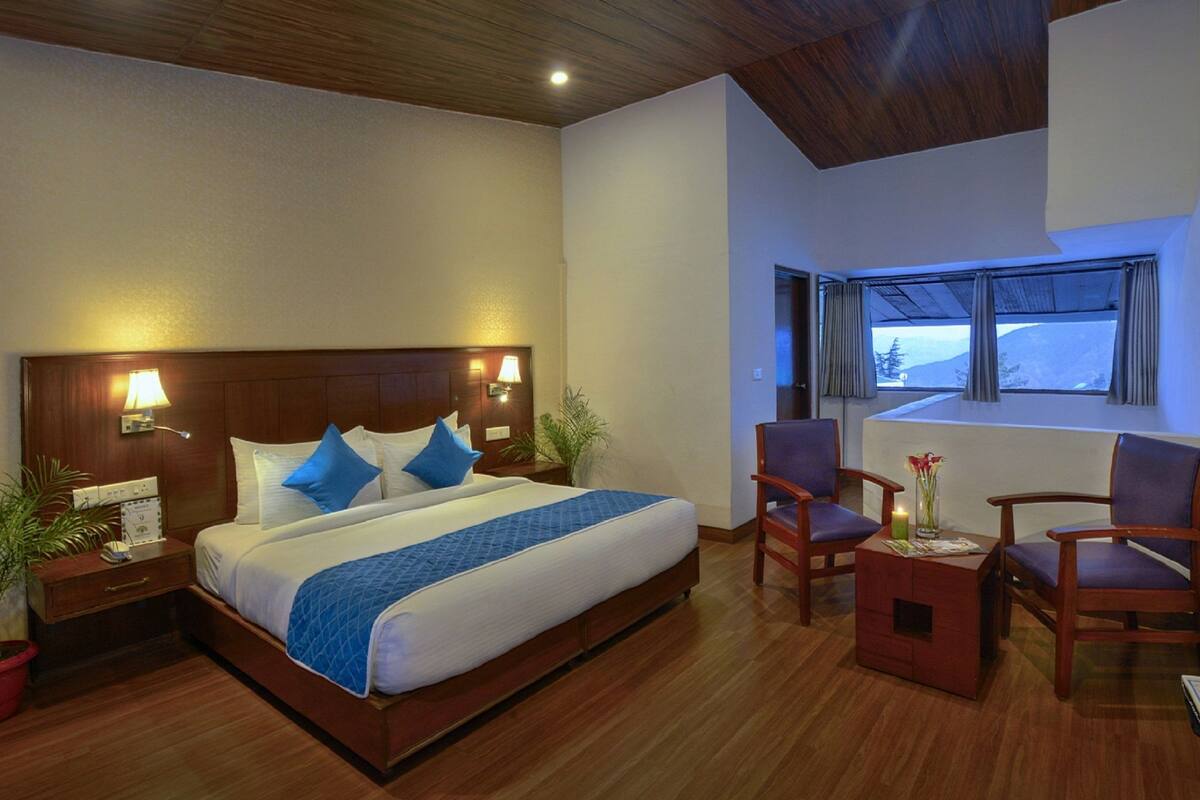 A hotel room with a large bed, two bedside tables, a desk with chairs, a TV, and a window with a view.