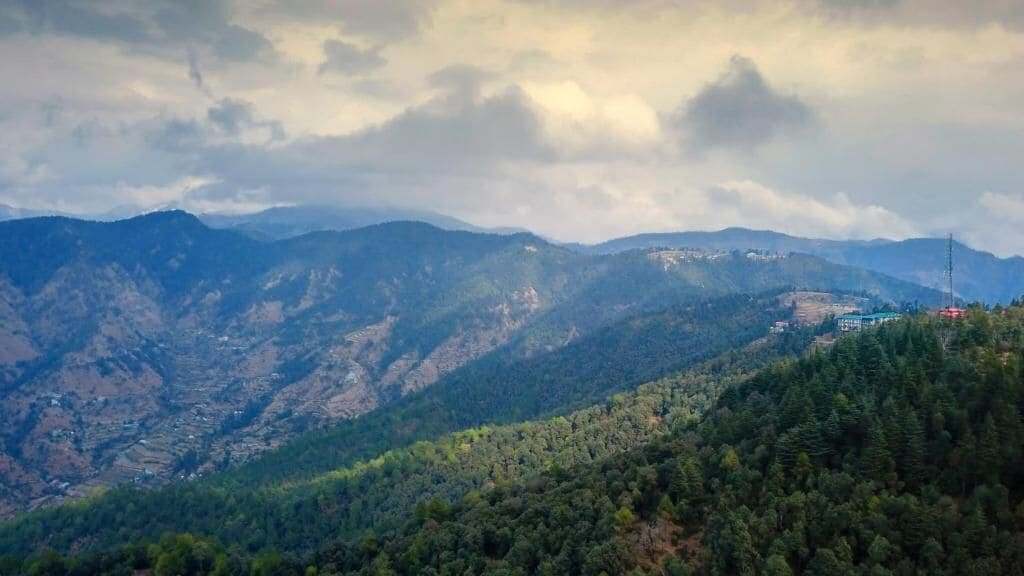 A mountainous landscape with dense forests and a few buildings in the distance.