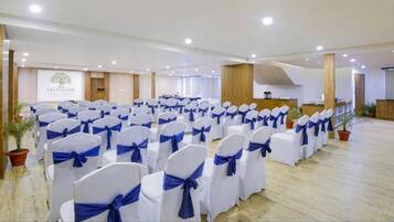 Une salle de conférence avec des rangées de chaises blanches ornées de rubans bleus, un pupitre en bois et une enseigne indiquant « Treehouse Chalet Villas ».