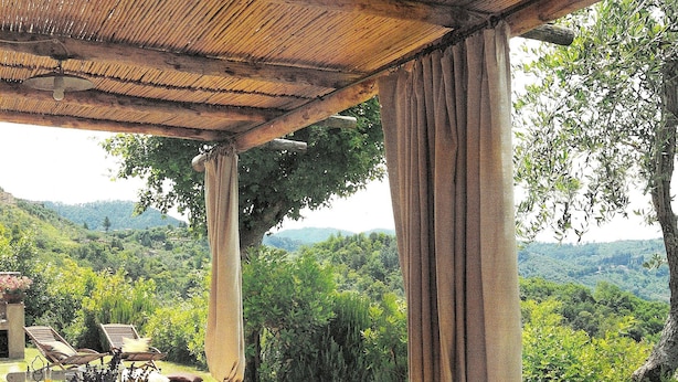 Un área de comedor al aire libre con una mesa dispuesta para una comida, rodeada de exuberante follaje y colinas al fondo.