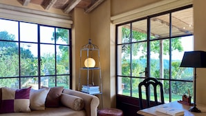 Una habitación acogedora con sofá, una mesa con lámpara, una lámpara de pie y ventanas amplias que dan a zonas verdes.