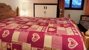 Un dormitorio con una cama grande, cabecera de madera, mesita de noche, ventana con vista a montañas nevadas y puerta con cerradura.