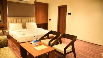 A hotel room with a bed, bedside table with water bottles, a chair, and a desk.