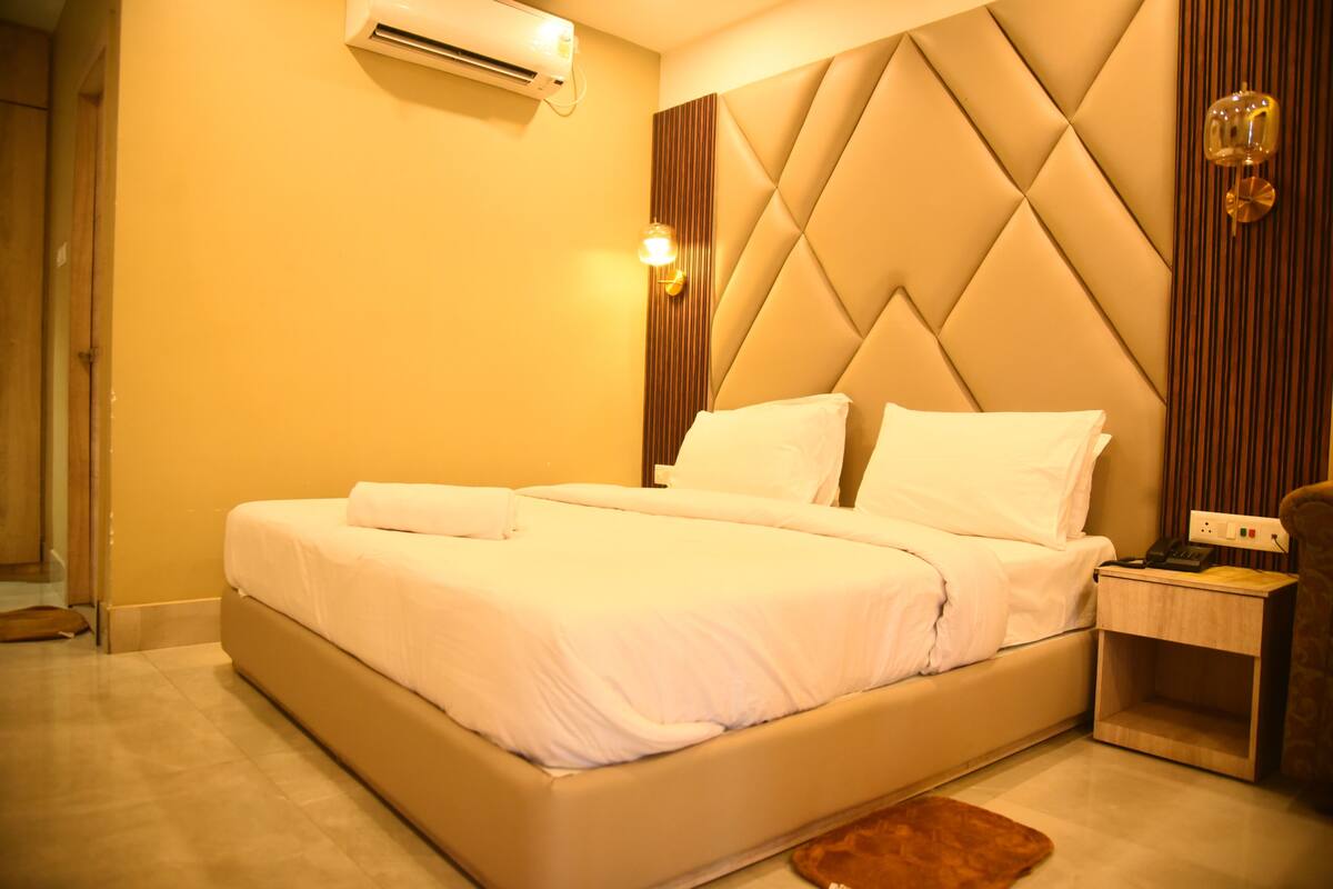 A hotel room with a bed, bedside table, and an air conditioning unit.