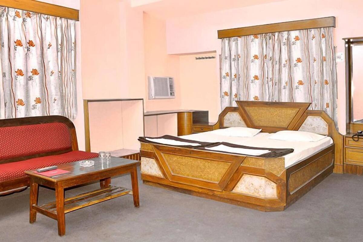 A hotel room with a wooden bed, a red sofa, a wooden table, and curtains with a floral pattern.