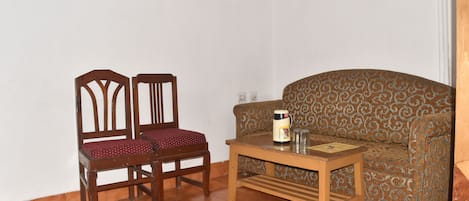 Una habitación con un sofá estampado, dos sillas de madera y una mesita de madera con una cafetera.