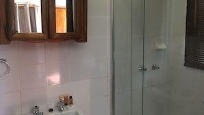 Een badkamer met een glazen douchecabine, een houten wastafelmeubel met spiegel, en een witte wastafel met toiletartikelen.