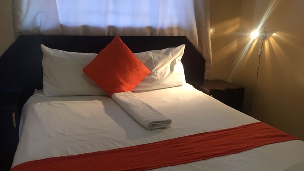 Een net opgemaakt bed met wit-oranje beddengoed, een opgerolde witte handdoek en een rode plaids.