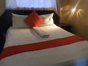 A neatly made bed with white and orange bedding, a rolled white towel, and a red throw blanket. - Namane Guest House (Ghanzi)
