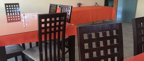 A dining area with a long table, several chairs, and a tablecloth.