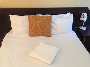 A neatly made bed with white and patterned pillows, a white towel, and a bedside table with a lamp. - Namane Guest House (Ghanzi)
