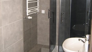 Casa de banho moderna com chuveiro em cabine de vidro, lavatório branco e barra para toalhas.