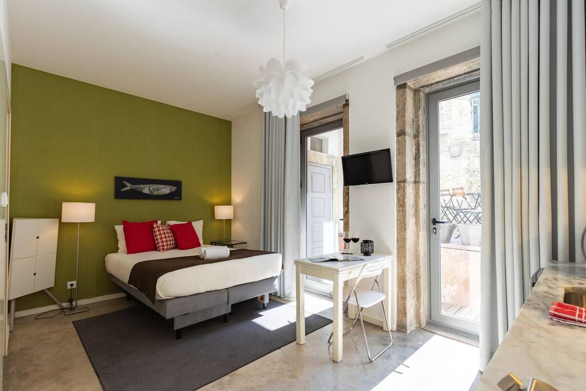 A modern hotel room with a bed, bedside tables, a desk, and a balcony with a view.