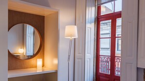 Ein Zimmer mit einer roten Tür, einem runden Spiegel, einer Stehlampe und einer gelben Bank.
