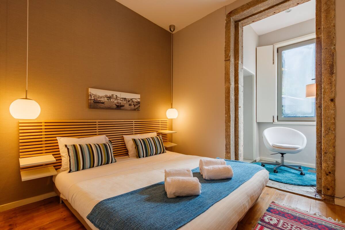 A hotel room with a bed, bedside lamps, a window, and a chair.