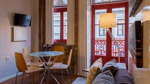 Ein gemütliches Zimmer mit Esstisch, Stühlen, einer Couch, einem Fernseher und einem Fenster mit roter Tür.