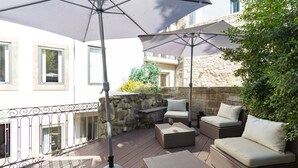 Ein Balkon mit Korbmöbeln, darunter eine Sitzecke mit einer Couch und zwei Stühlen, unter einem großen Sonnenschirm.