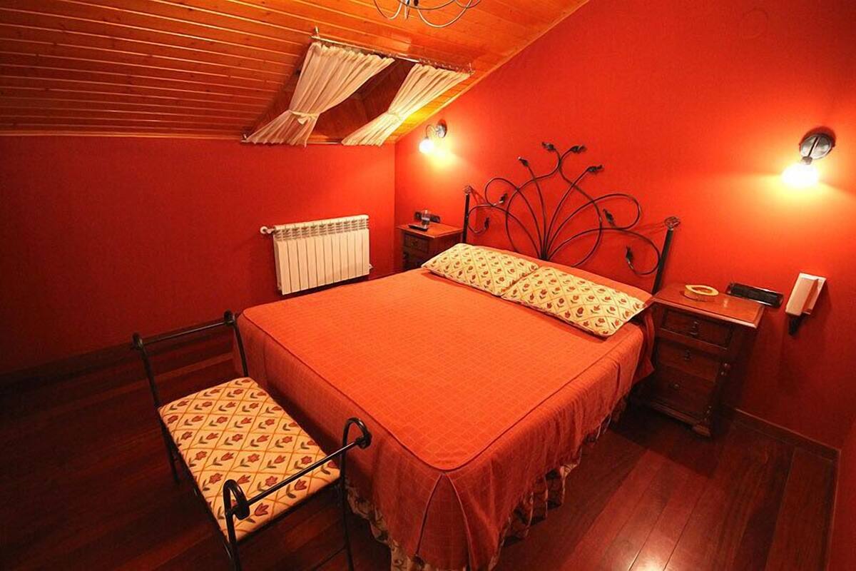 Een slaapkamer met een bed, nachtkastje, stoel, radiator en een wandlamp.