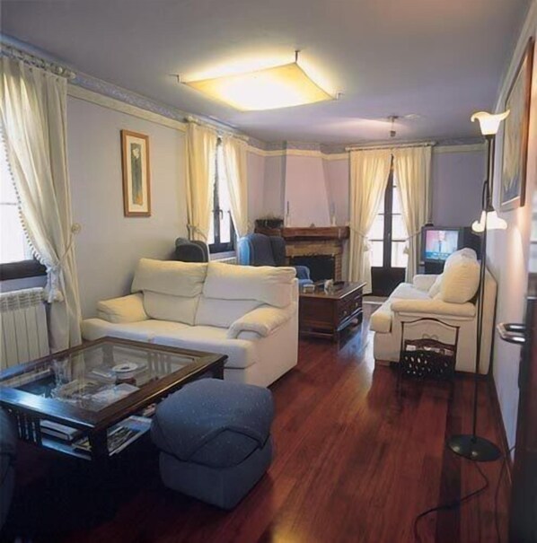 A living room with a white sofa, a blue armchair, a glass coffee table, and a fireplace. - Hotel Casa Suarna (Navia de Suarna)
