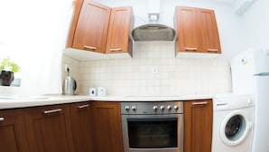 Eine Küche mit Holzausstattung, einem Edelstahlbackofen, einer Waschmaschine und einer gefliesten Spritzschutzwand.