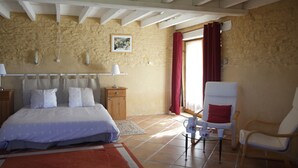 Un dormitorio con cama, mesitas de noche, una silla, una mesa y una ventana con cortinas.