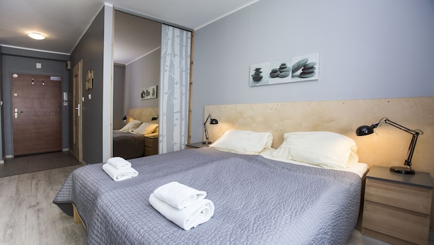 Uma cama bem arrumada com cobertura acolchoada, duas luminárias de cabeceira e uma mesa de cabeceira de madeira.