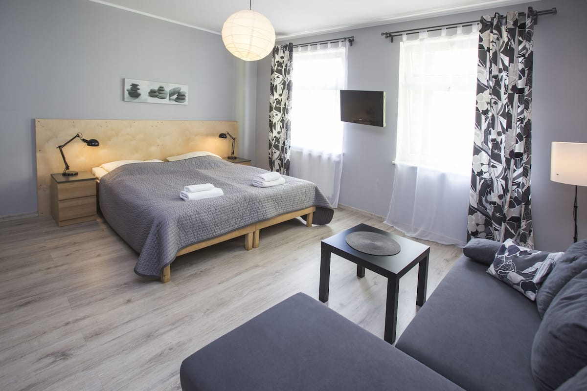 Ein modernes Schlafzimmer mit einem Bett, Nachttischen, einem kleinen Tisch, einer Couch und einem Fernseher.
