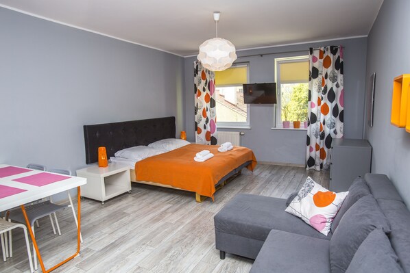 A modern bedroom with a bed, a sofa, a desk, and a TV. - Apartamenty Sedinium - Brama Portowa (Szczecin)