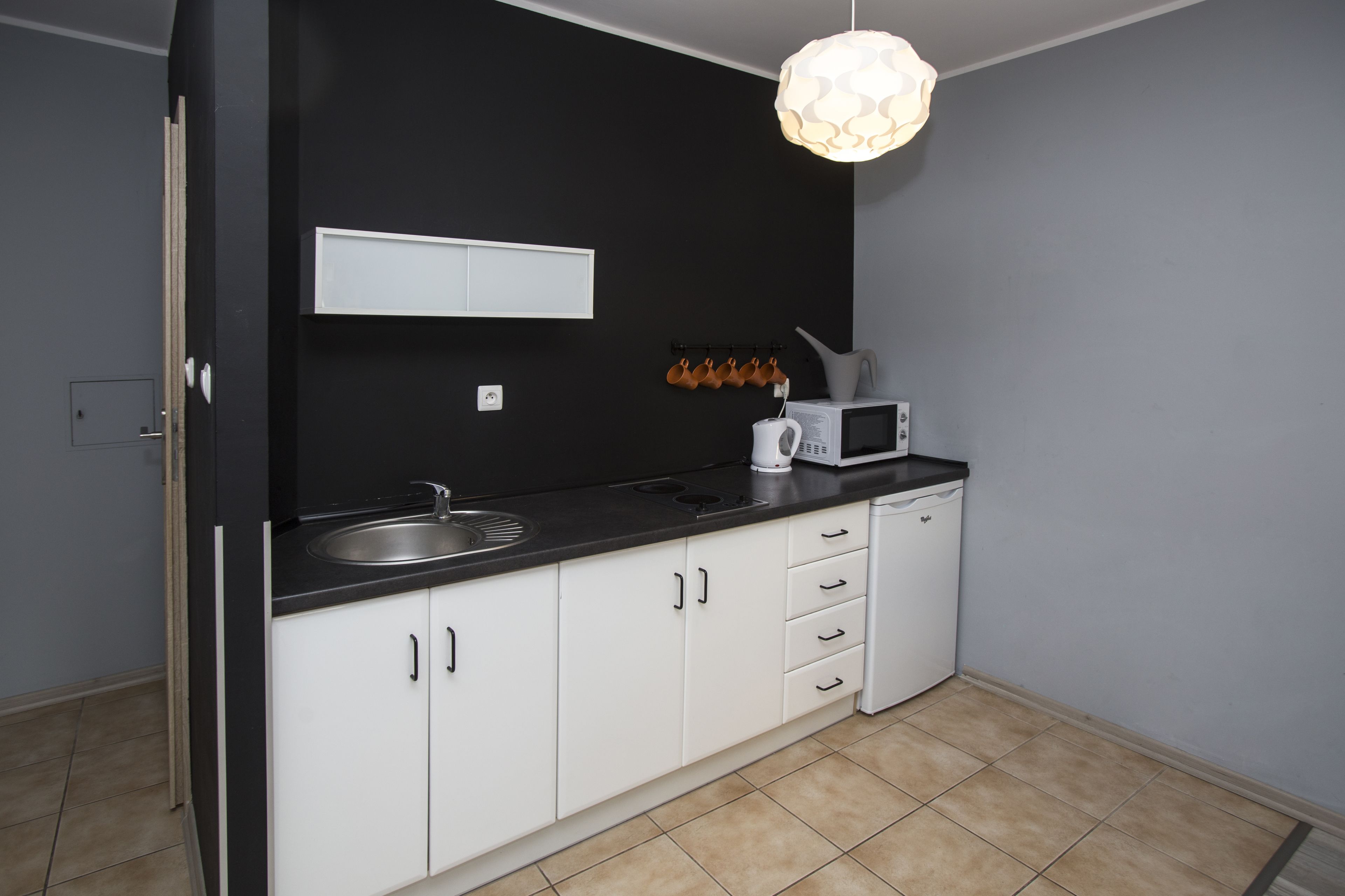 A modern kitchen with white cabinets, a black countertop, a microwave, and a hanging light fixture.