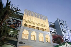 A hotel with a modern design, featuring a prominent glass facade and multiple balconies. - Our Nomad Boutique Hostel (Phuket)