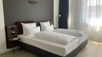 Una habitación de hotel moderna con una cama grande, una mesita de noche, una lámpara y vistas al exterior a través de cortinas traslúcidas.