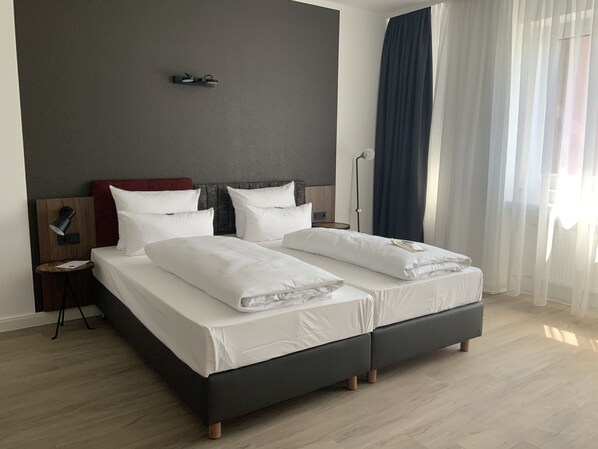 Habitación de hotel moderna con una cama grande, una mesita de noche, una lámpara y vistas al exterior.