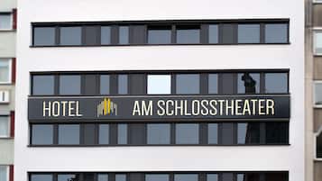 Un letrero de hotel con el nombre 'HOTEL AM SCHLOSSTHEATER' en la fachada de un edificio moderno.